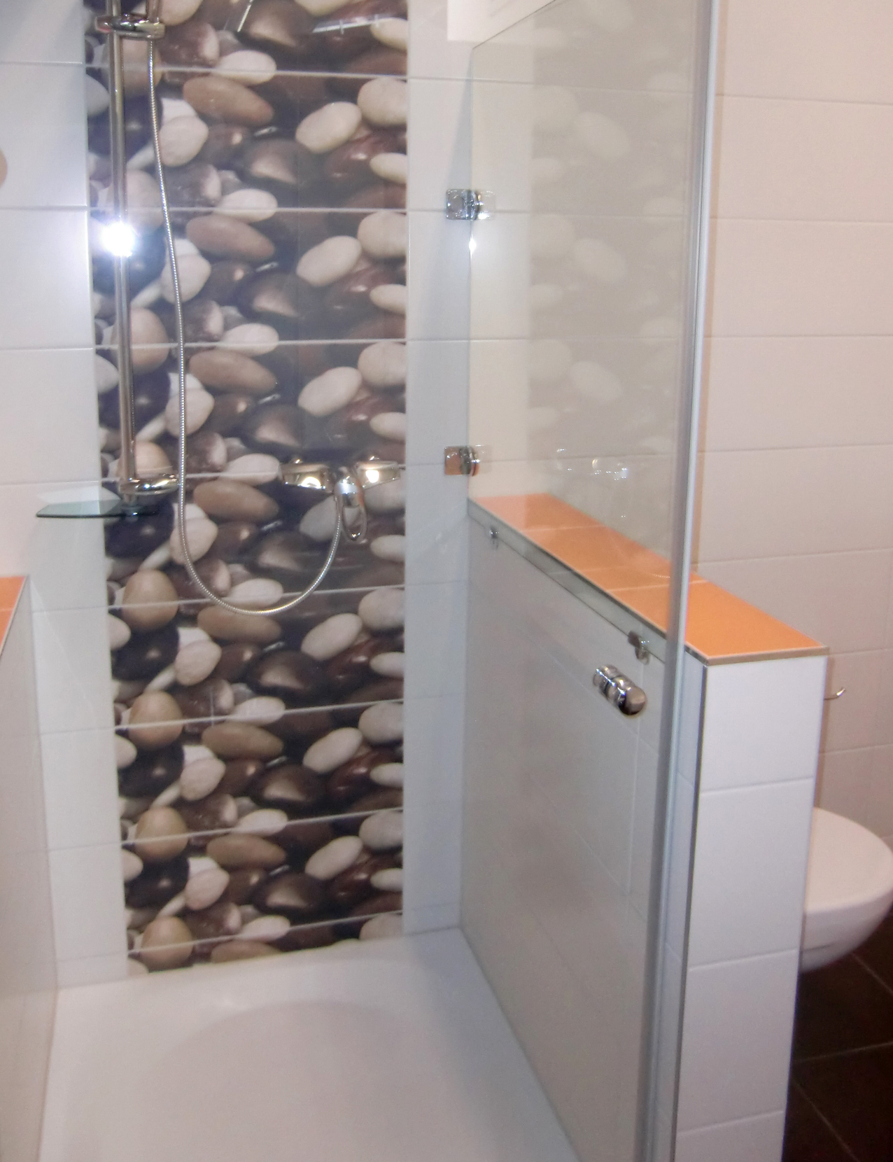 Modernes Badezimmer weiß gefliest, aufgelockert mit farbigen, orangen und schwarzen Fliesen, Duschkabine mit dekorativen Steinen